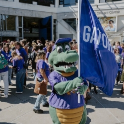 Alli Gator on campus holding Gators flag with students in background